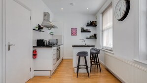 Una cocina compacta con armarios blancos, estufa integrada y una pequeña isla con taburetes.