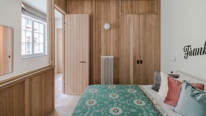A bedroom with a wooden wardrobe, a radiator, a bed with patterned bedding, and a wall with the name 'Frank'. - Casa Peppino - Soho - by Frankie Says (London)