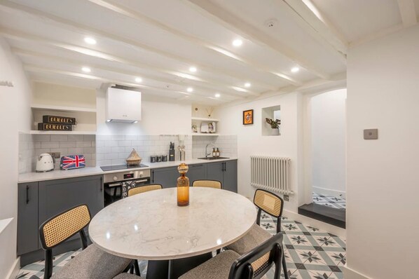 A modern kitchen with a round dining table, grey cabinets, and a white ceiling with recessed lighting. - Pottter s Perch - Covent Garden - by Frankie Says (London)