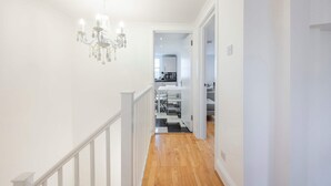 A hallway with a chandelier, a staircase, and a view into a kitchen area.