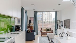 Un appartement moderne comprenant une cuisine, un espace de vie et un coin repas. Il est doté d’une grande fenêtre avec des rideaux, d’un canapé, d’une table basse et d’une table à manger avec des chaises.