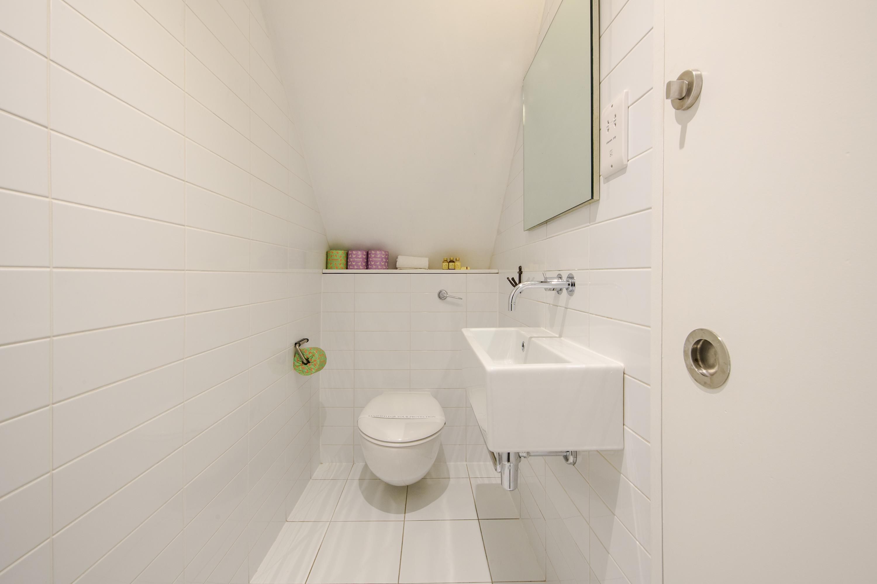 A small, white bathroom with a toilet, sink, and mirror.