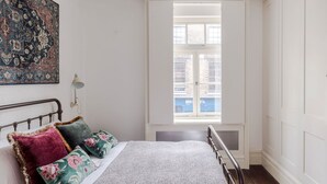 Une chambre à coucher avec un lit, des oreillers, une fenêtre et une œuvre d’art accrochée au mur.