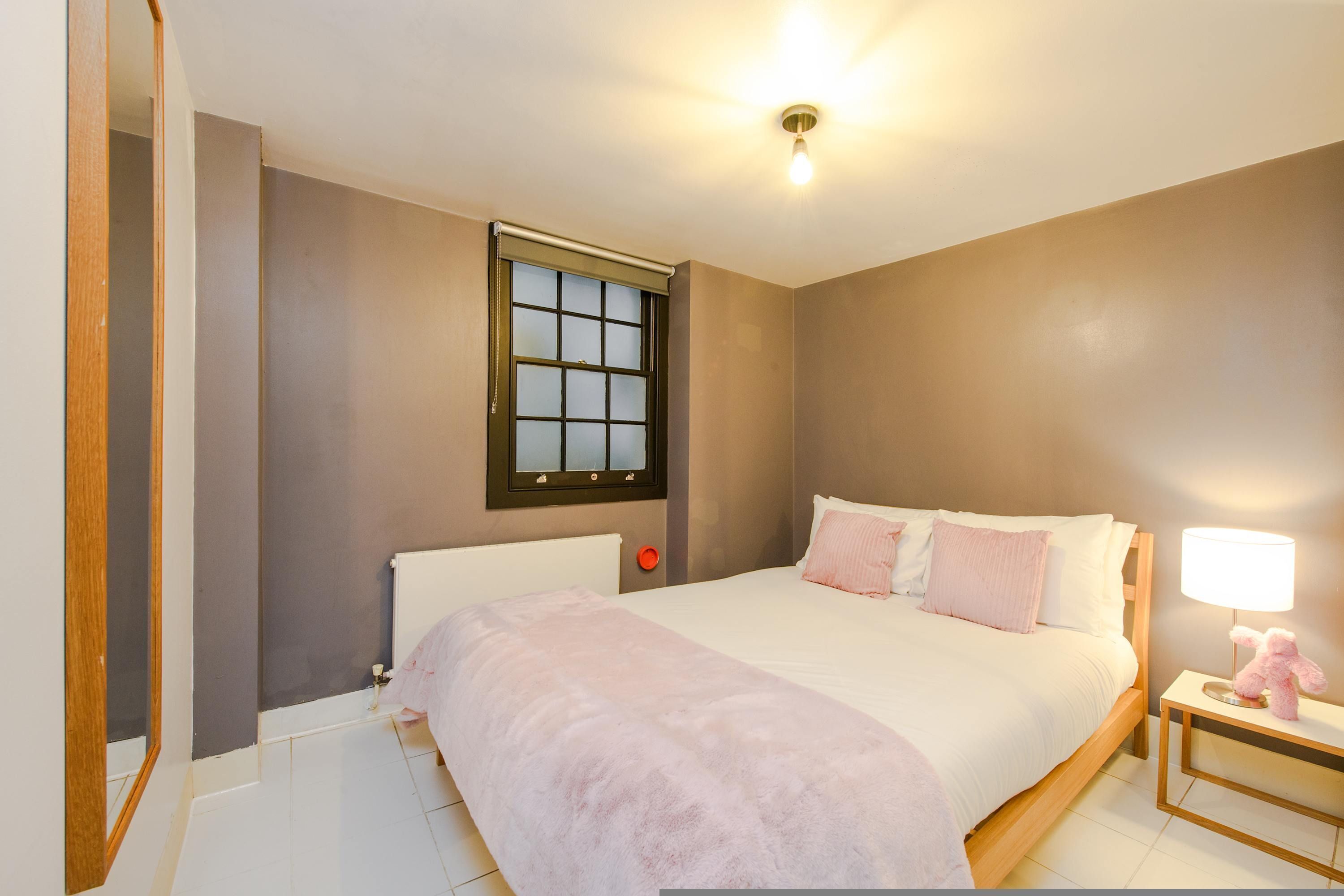 Een slaapkamer met een groot bed, een nachtkastje met een lamp en een raam met jaloezieën.