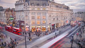 A historic building with classical architecture, a prominent Christmas sign, and a busy street with double-decker buses.