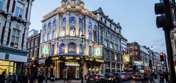 Um edifício histórico com um canto curvo notável, janelas amplas e sinalização iluminada para um teatro.