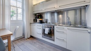 A modern kitchen with stainless steel appliances, a window with white curtains, and a wooden table. - The Foxhole - Fitzrovia - by Frankie Says (London)