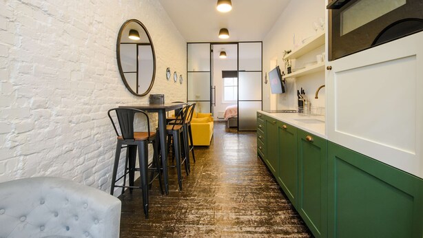 A compact kitchen with a white brick wall, a dining area with a yellow sofa, and green cabinets.