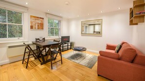 A living room with a dining table, chairs, a TV, a sofa, and a large window. - The Play Pen - Holborn - by Frankie Says (London)