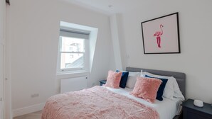 A bedroom with a large bed, a window, a framed picture of a flamingo, and a bedside table with a lamp. - Soul in the City - Fitzrovia - by Frankie Says (London)