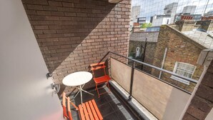 Ein Balkon mit einer Ziegelwand, einem kleinen Tisch und zwei orangefarbenen Stühlen.