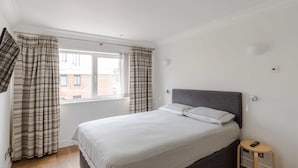 Un dormitorio con cama, cortinas, una mesita de noche y una ventana.