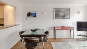 Una sala de estar moderna con una mesa de vidrio, sillas negras, una mesa de centro de madera, un televisor de pantalla plana y un cuadro abstracto enmarcado en la pared.