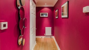 Un pasillo con una pared roja, una puerta blanca y un radiador.