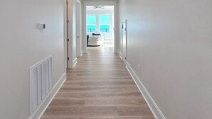 A hallway with a wooden floor, white walls, and a view to a balcony with a white chair. - Seaside Villa - Gulf Breeze with an Ocean View! (Long Beach)