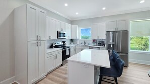 A modern kitchen with white cabinetry, stainless steel appliances, and a central island with bar stools. - Seaside Villa - Gulf Breeze with an Ocean View! (Long Beach)