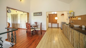 A spacious kitchen with wooden flooring, a dining area with a wooden table and chairs, and a kitchen counter with a sink and various appliances. - Samrakshitha Suits  (Kotagiri)