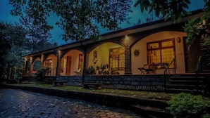 A building with a stone facade, arched windows, and a paved entrance area. - Samrakshitha Suits  (Kotagiri)
