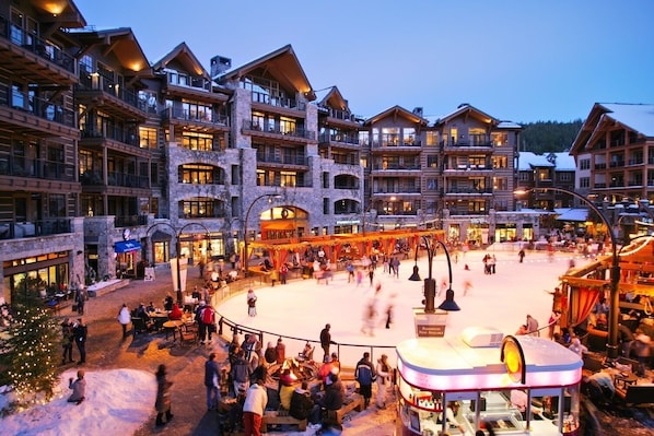 Un hotel de varios pisos con un patio central que cuenta con una pista de hielo, asientos al aire libre y un puesto de comida.
