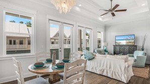 A spacious living room with a dining area, large windows, a ceiling fan, and a view of the outside. - 🔆 Golf Cart | Bikes | The Big Chill | Resort Pools ​​​​​​ (Inlet Beach)