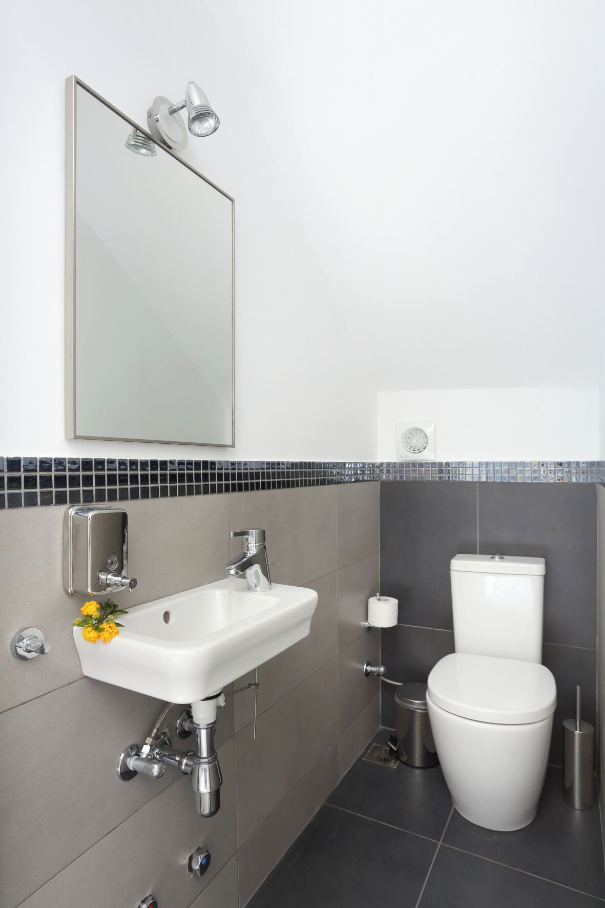 A modern bathroom with a white sink, chrome fixtures, a toilet, and a mirror.