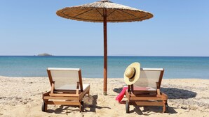 Two wooden lounge chairs with mesh backs facing a beach with a clear view of the sea and a distant island. - Aithra Andros (Andros)