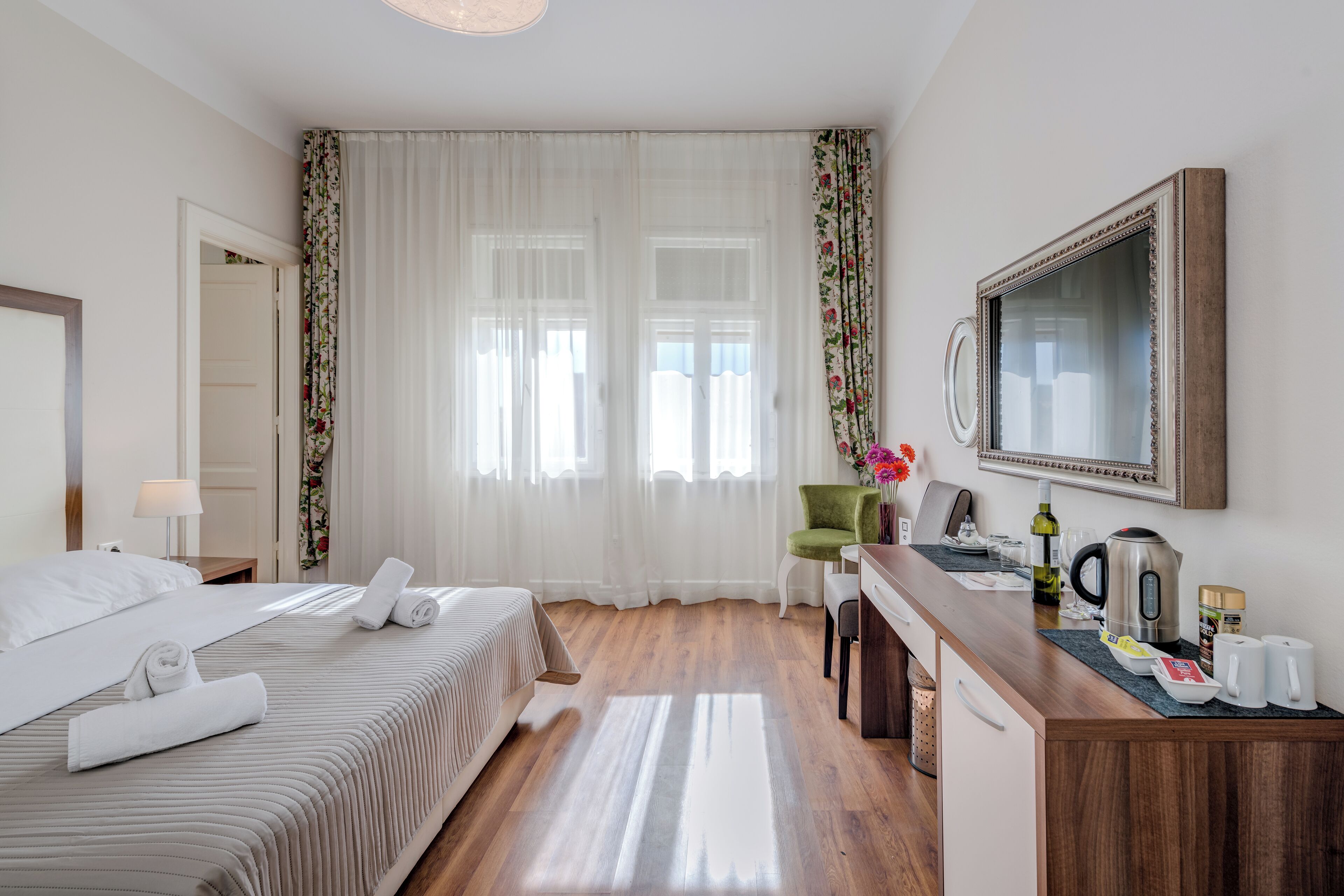 Una habitación de hotel con cama, escritorio, silla, espejo y ventana con cortinas.