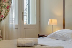 A hotel room with a bed, a nightstand, a lamp, and a door with a window. - Bastion Luxury Rooms (Split)