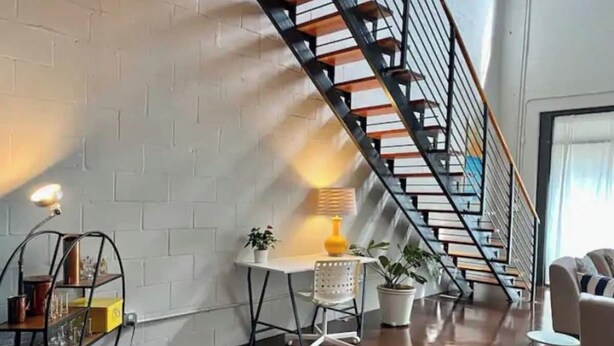 A modern living room with a staircase, a white brick wall, and a wooden floor. - Amazing Loft in Historic Springfield (Jacksonville)