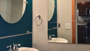 A bathroom with a large oval mirror, a sink, and vanity lights. - Amazing Loft in Historic Springfield (Jacksonville)
