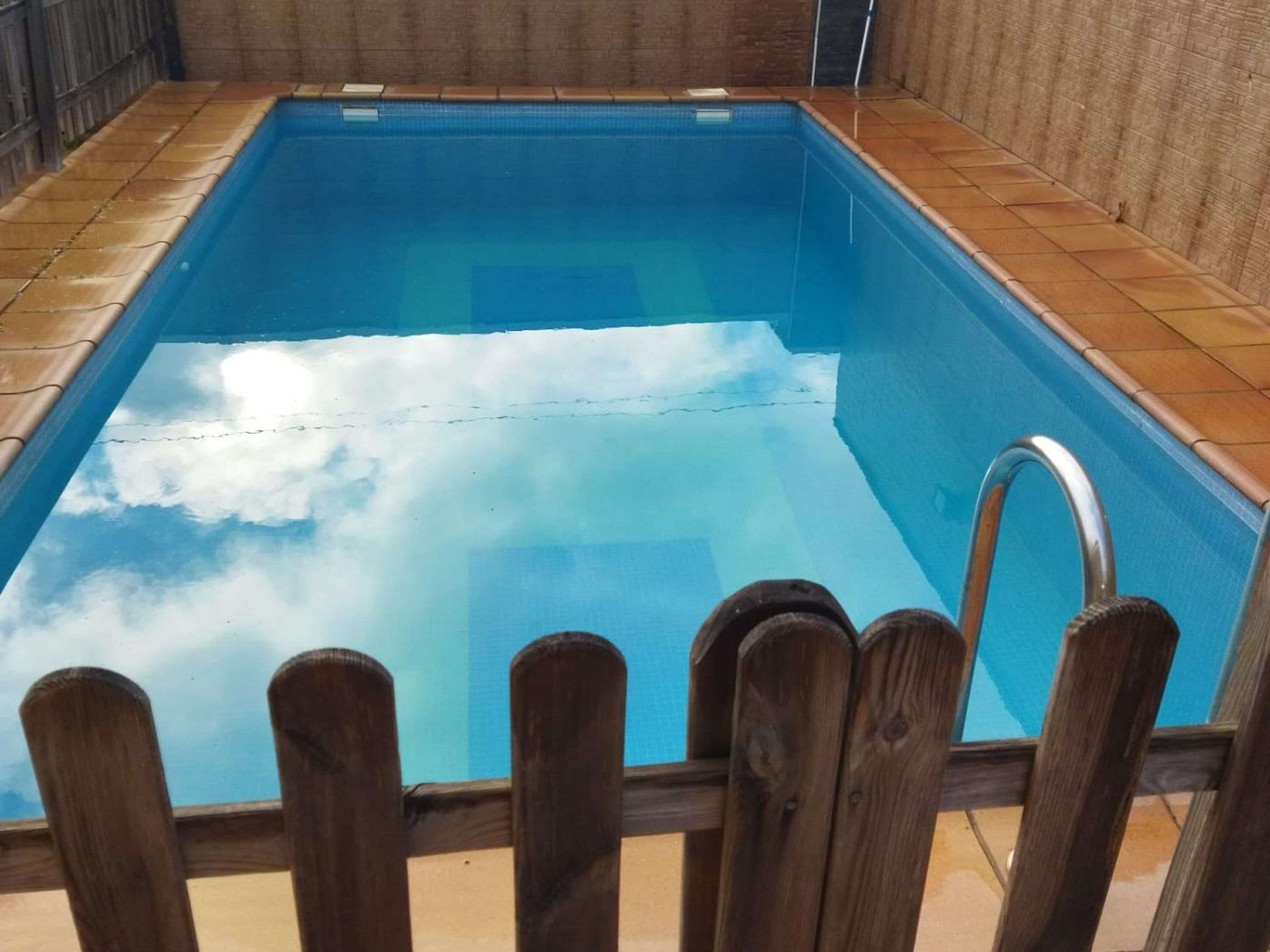 A rectangular swimming pool with a wooden fence in the foreground.