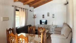A cozy living room with a wooden ceiling, a dining table with chairs, a sofa, a TV, and a cabinet with decorative items. - Casa Antonio III 113 (Conil de la Frontera)