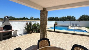 A patio with a stone pillar, a grill, and a pool area with lounge chairs. - Casa Antonio III 113 (Conil de la Frontera)