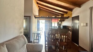 A cozy living room with a wooden ceiling, a sofa, dining chairs, and a kitchen area with a microwave. - Casa Antonio III 113 (Conil de la Frontera)