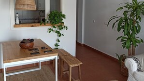 Una habitación con una mesa de madera, un banco, una lámpara de mimbre colgante, una planta en maceta y un sofá blanco.