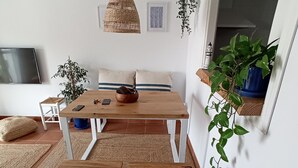 Un salón acogedor con una mesa de madera, bancos, televisor y plantas en macetas.