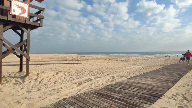 Un muelle de madera que da a una playa, con un puesto de salvavidas a la izquierda.