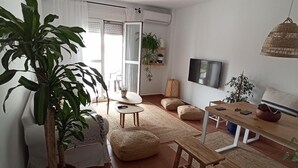Una sala de estar moderna con una planta grande, un sofá, una mesa de centro y un televisor montado en la pared.