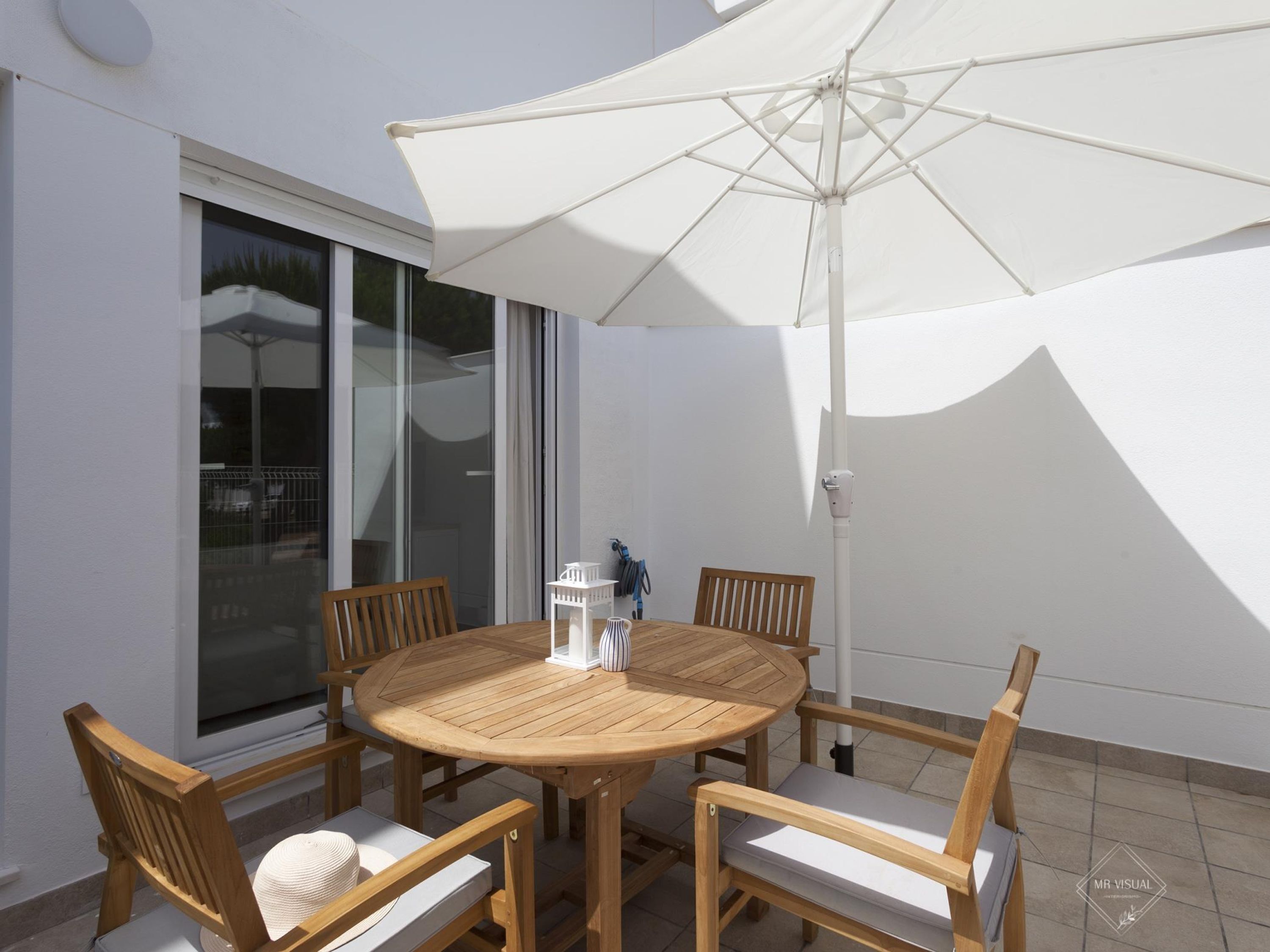 A round wooden table with four chairs, a white umbrella, and a small white table lamp.