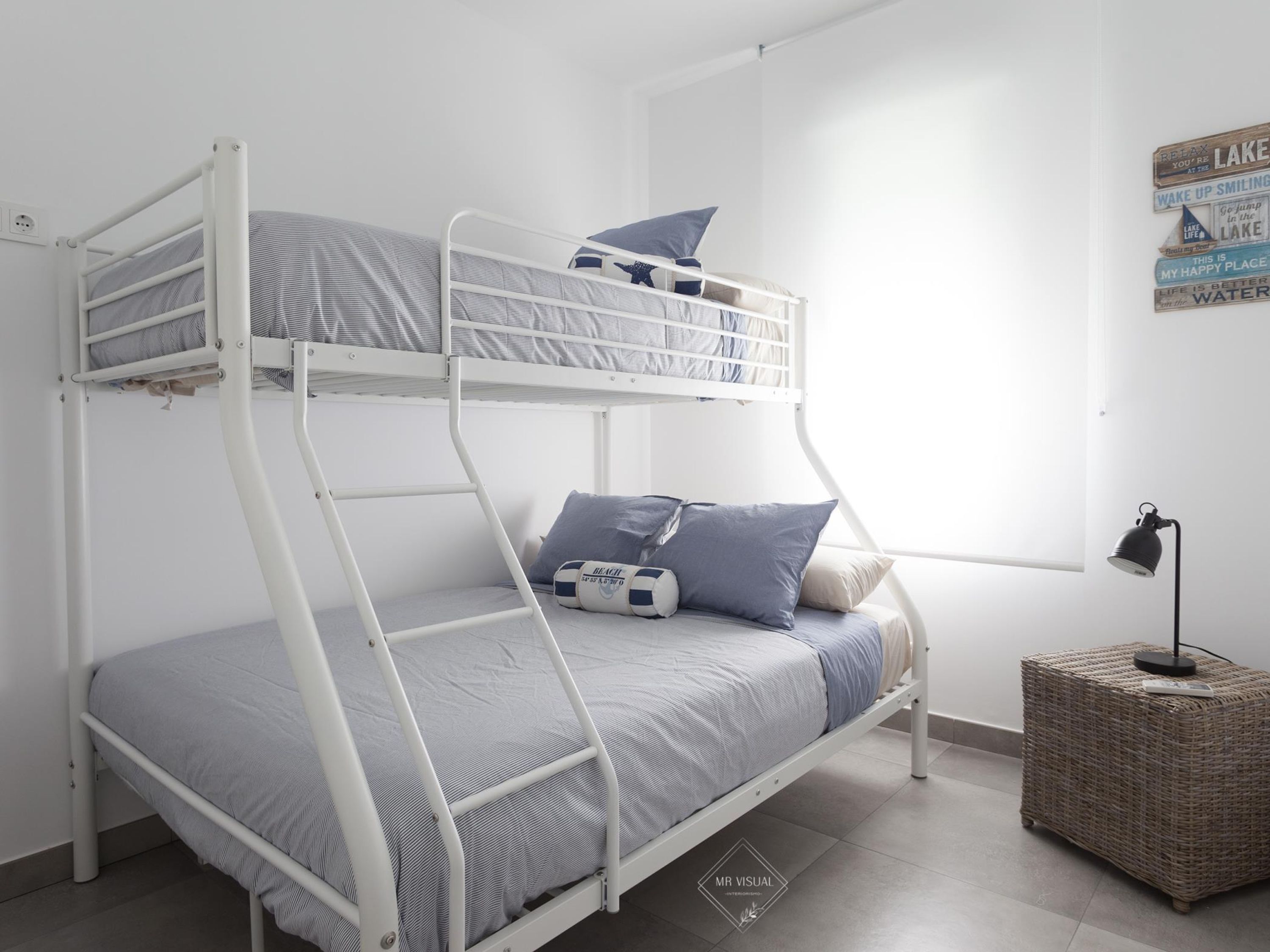 Uma cama beliche com uma cama inferior, uma mesinha de cabeceira com luminária e uma parede com mensagens motivacionais.