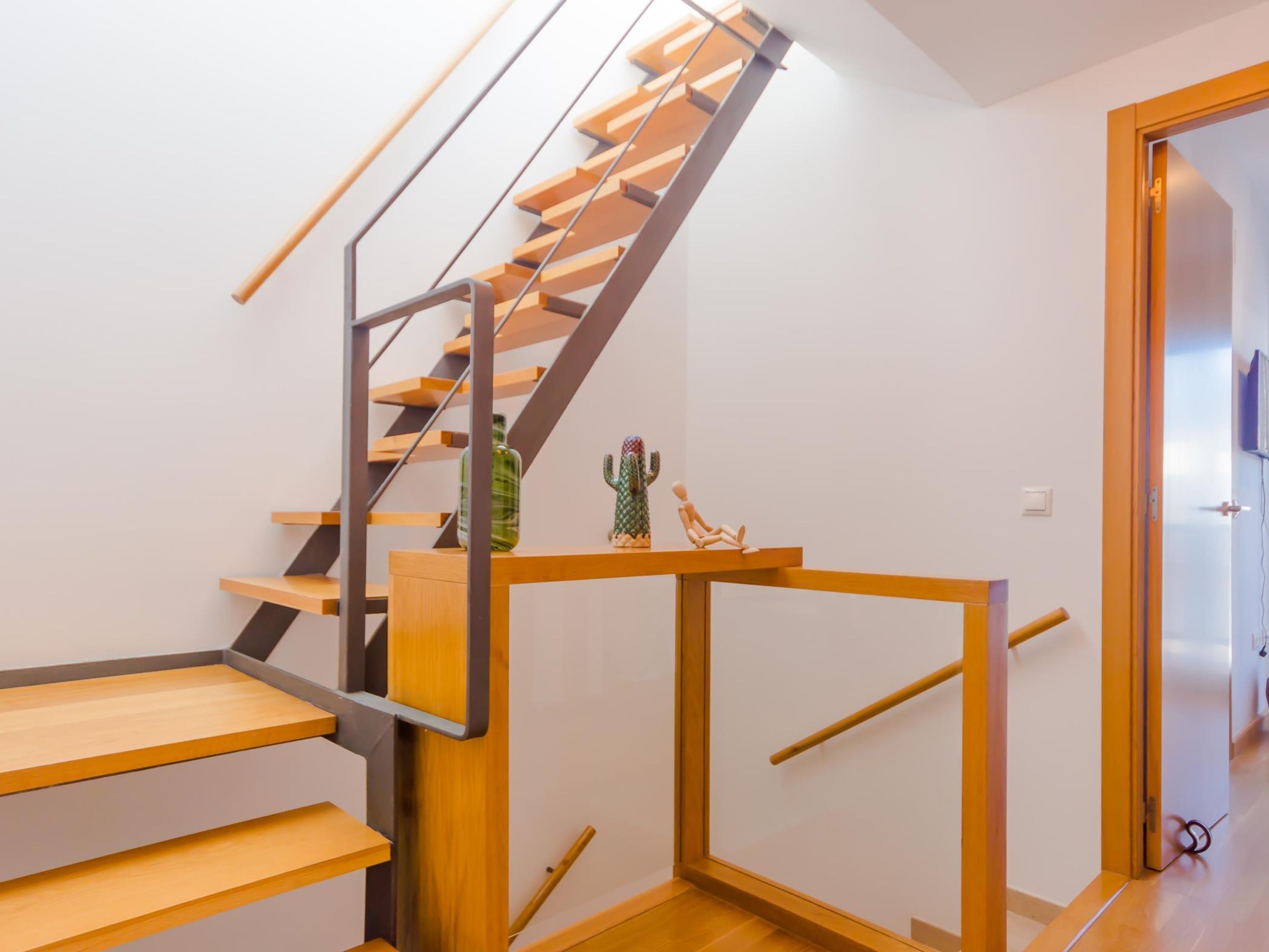 A modern staircase with wooden steps and metal railings, leading to a room with a wooden floor and a door.