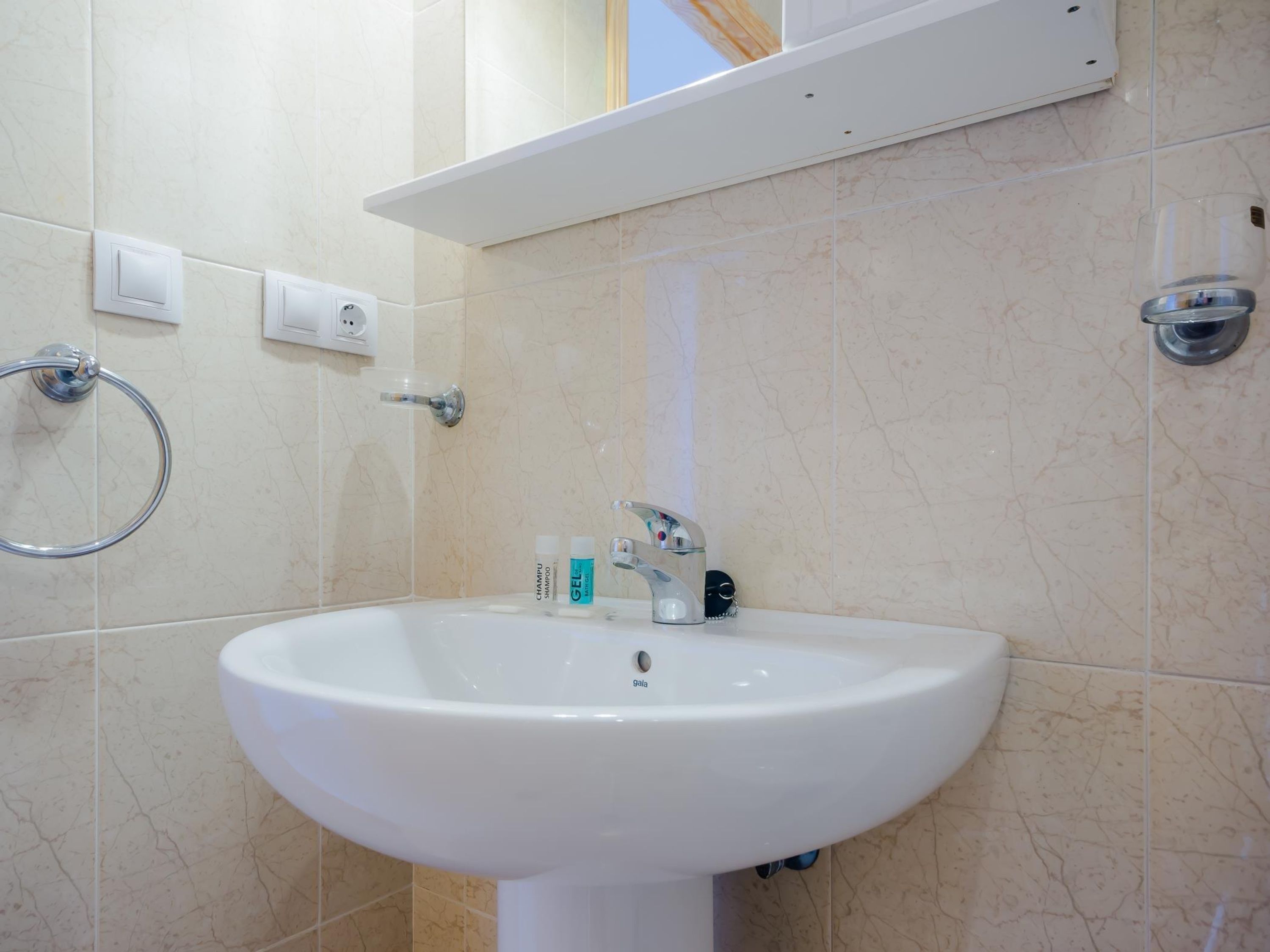 A bathroom with a white sink, a towel ring, and a shelf above the sink.