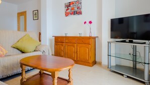 Un salon comprenant un canapé, un meuble en bois, un meuble TV en verre et un téléviseur à écran plat.