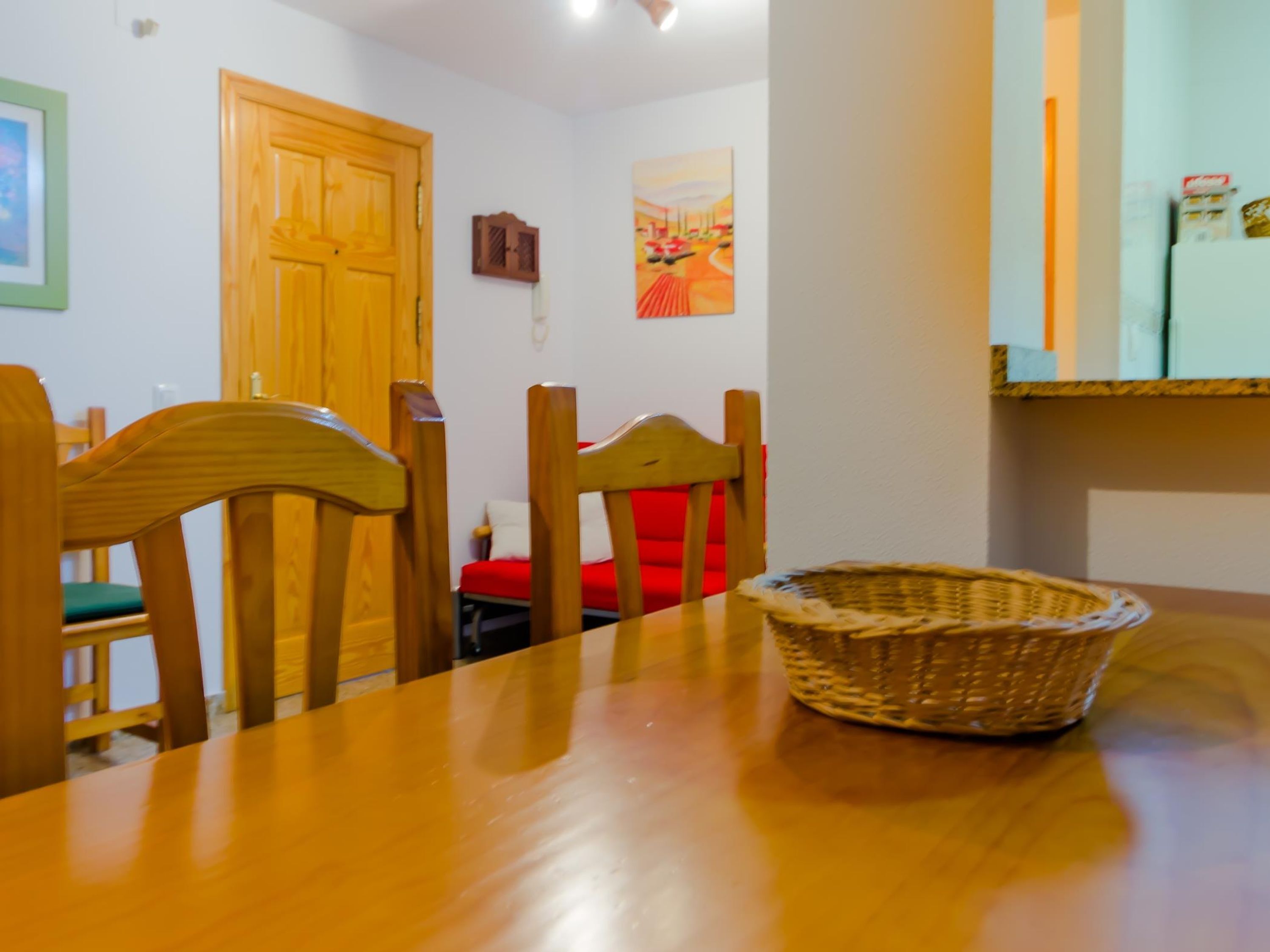Un coin repas avec une table en bois, des chaises, un panier en osier et une chaise rouge.