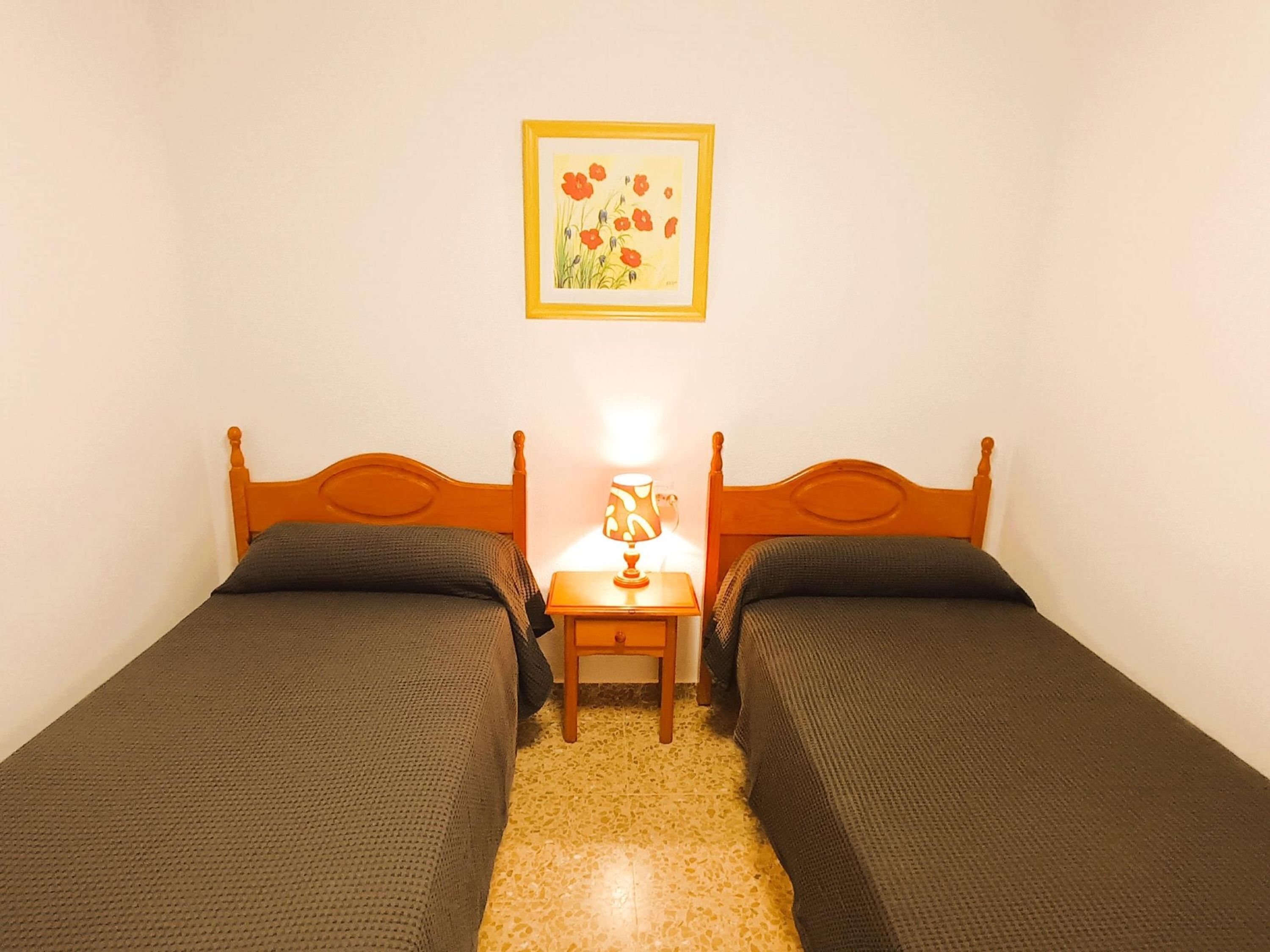 A room with two single beds, a nightstand with a lamp, and a framed picture on the wall.
