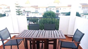 A balcony with a wooden table and four chairs, surrounded by white walls and a view of buildings. - Apartamento Canela 2536 (Conil de la Frontera)