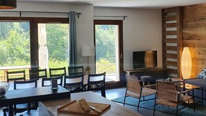 A modern room with a dining area, a TV, and large windows offering a view of the outdoors.