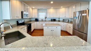 Una cocina moderna con armarios blancos, encimeras de granito y electrodomésticos de acero inoxidable, con una isla central.