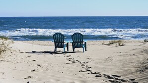 Dos sillas Adirondack mirando al océano sobre una playa arenosa.