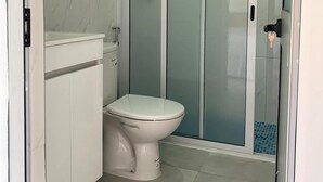 A bathroom with a toilet, a cabinet, and a shower enclosure. - Laranjinha Rooms (Paul)